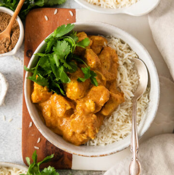 A spoon in a bowl of Indian butter chicken and rice.