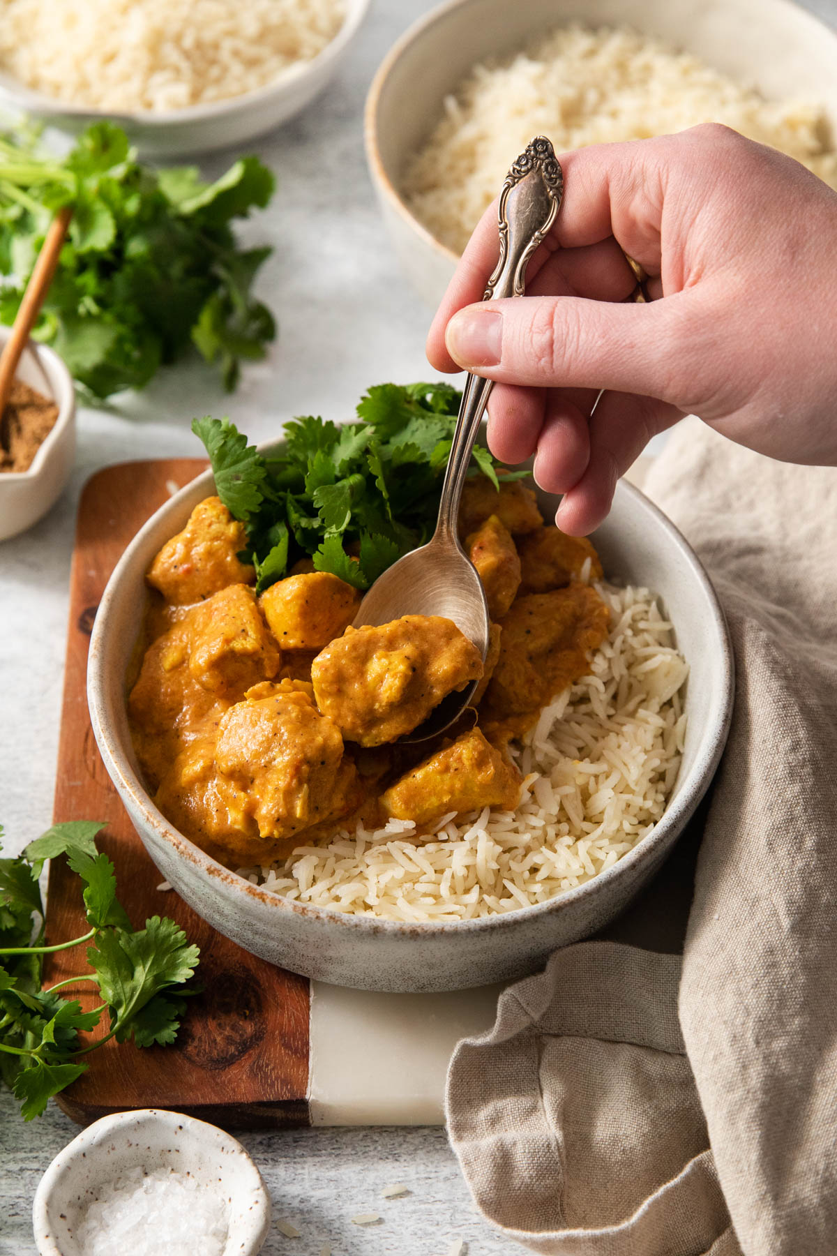 A hand scooping up butter chicken with a spoon.