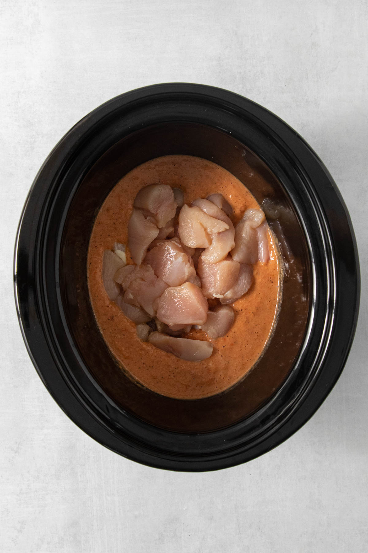 Adding chicken pieces to butter chicken sauce in a slow cooker.