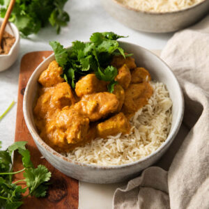 An image of slow cooker butter chicken in a bowl with basmati rice and cilantro.