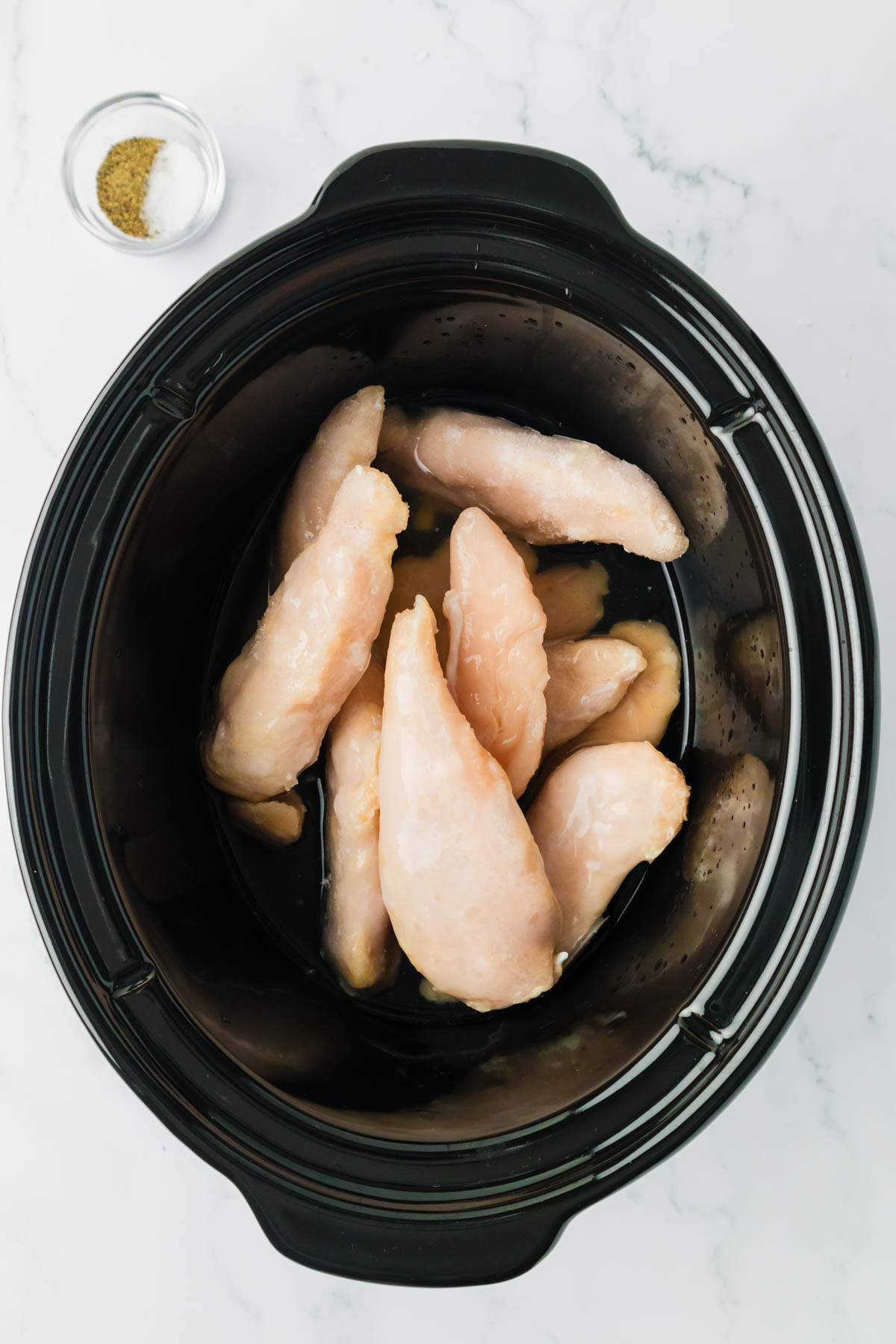 Frozen chicken breasts in a slow cooker with chicken broth and seasonings.