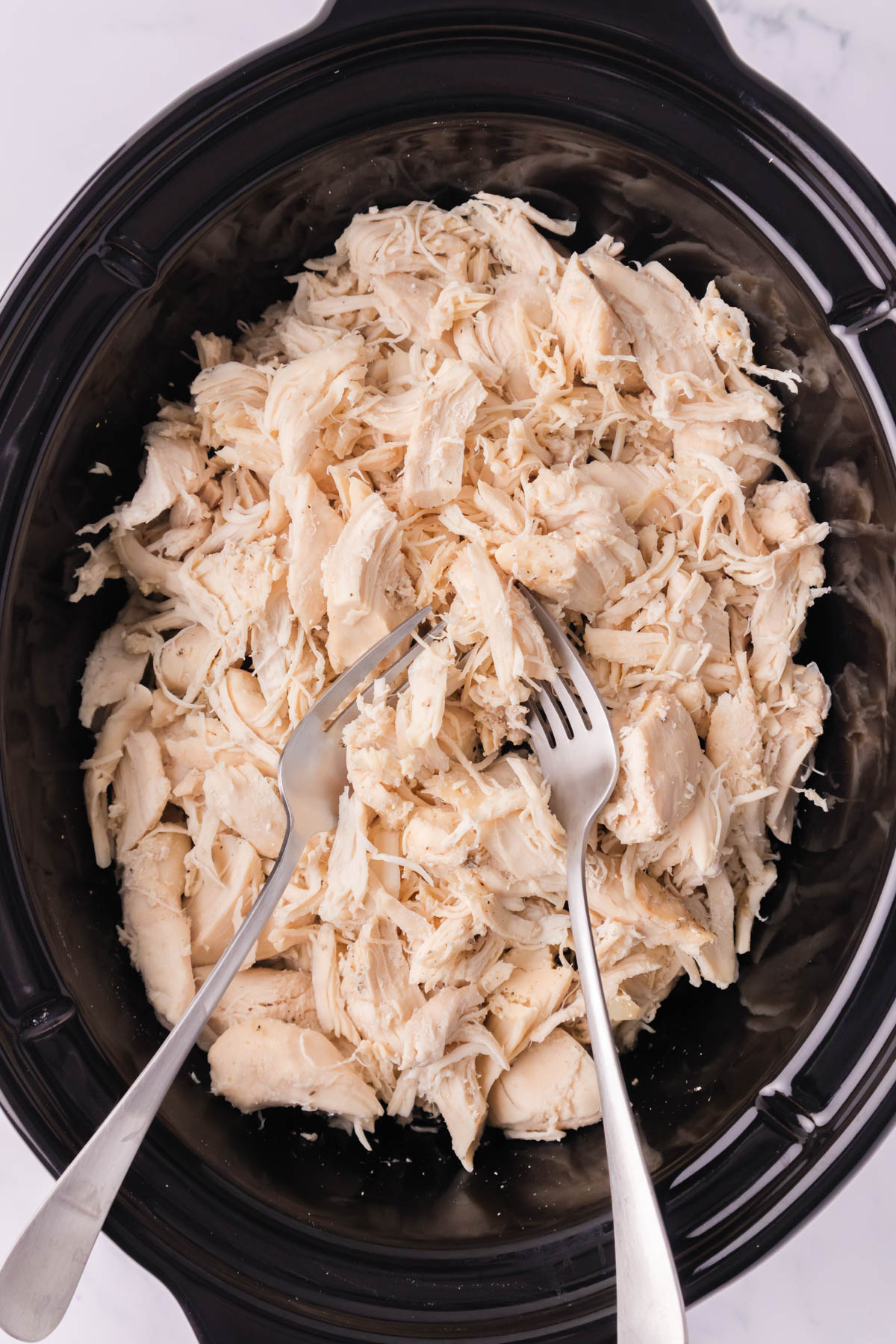 An overhead image of cooked shredded chicken in a crock pot with two forks.