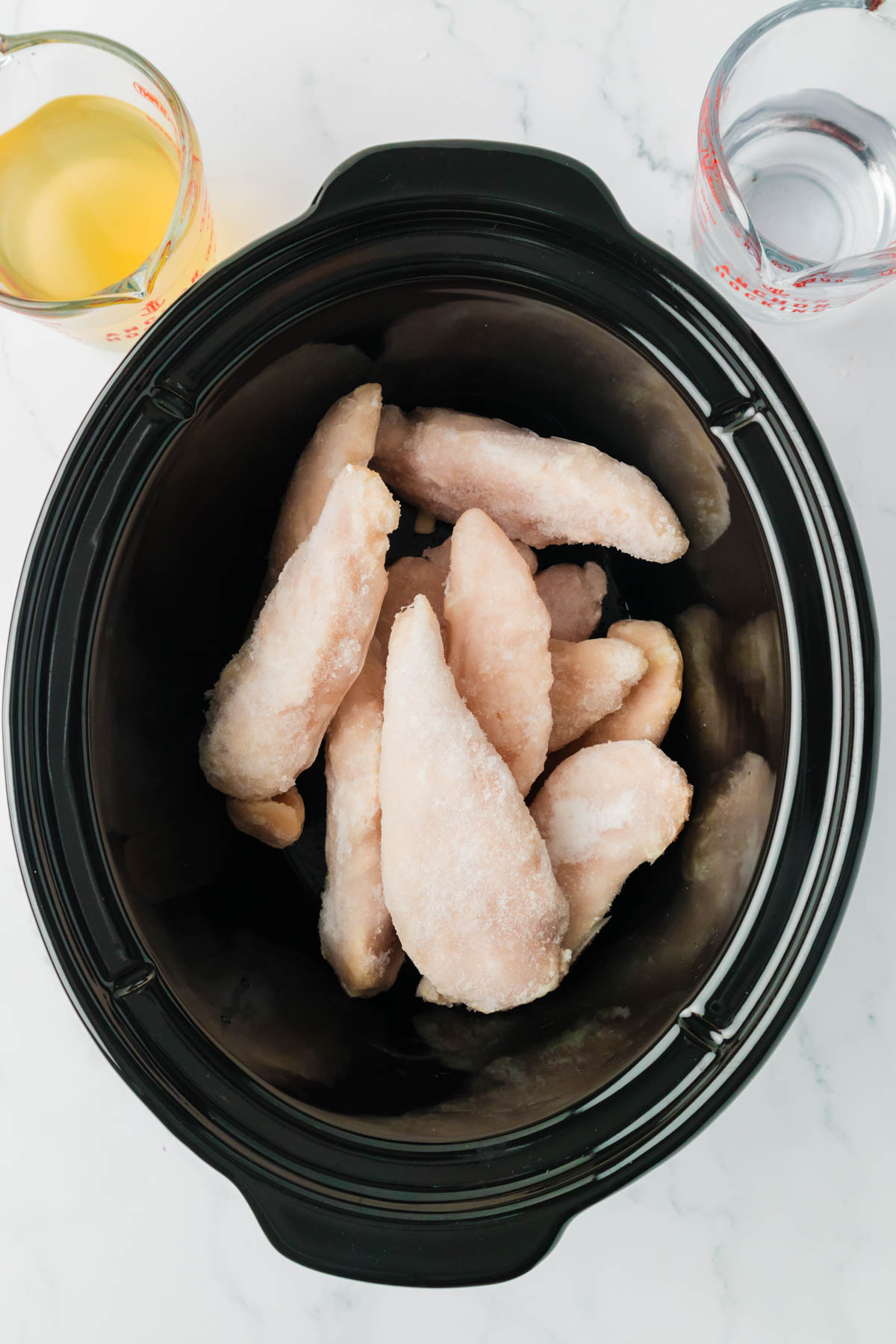 Adding frozen chicken to a slow cooker.