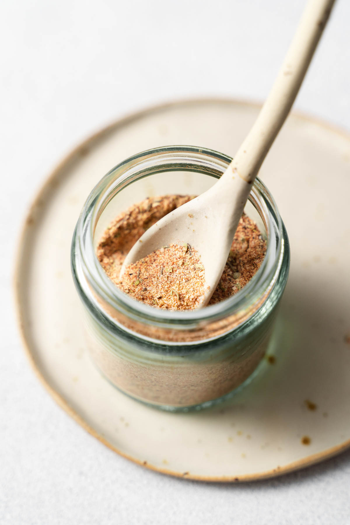 A close up image of a glass jar containing spices, with a spoon inserted into the spice blend.
