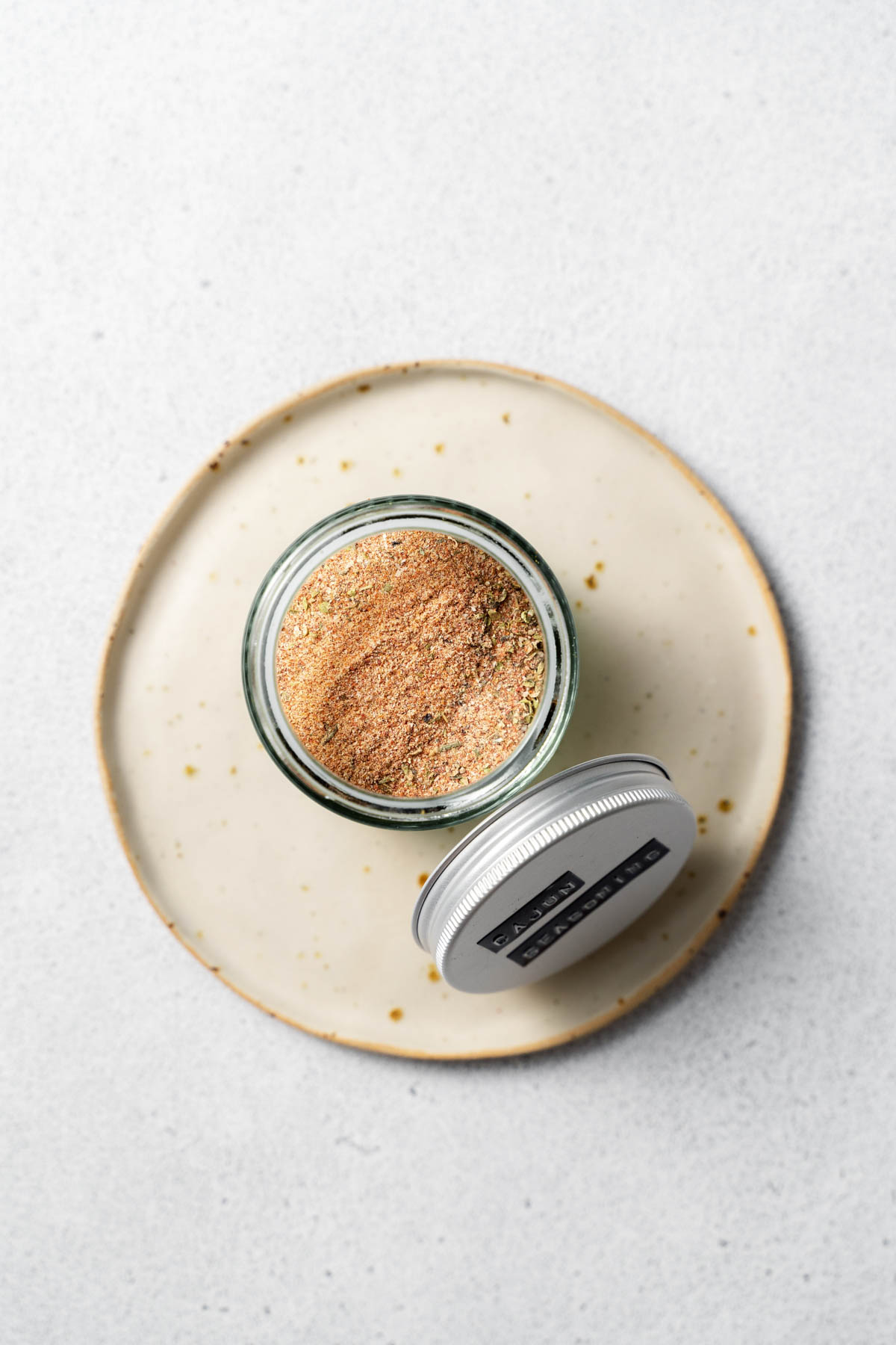 Overhead image of a cajun seasoning in a glass jar, with a lid resting against the jar. 