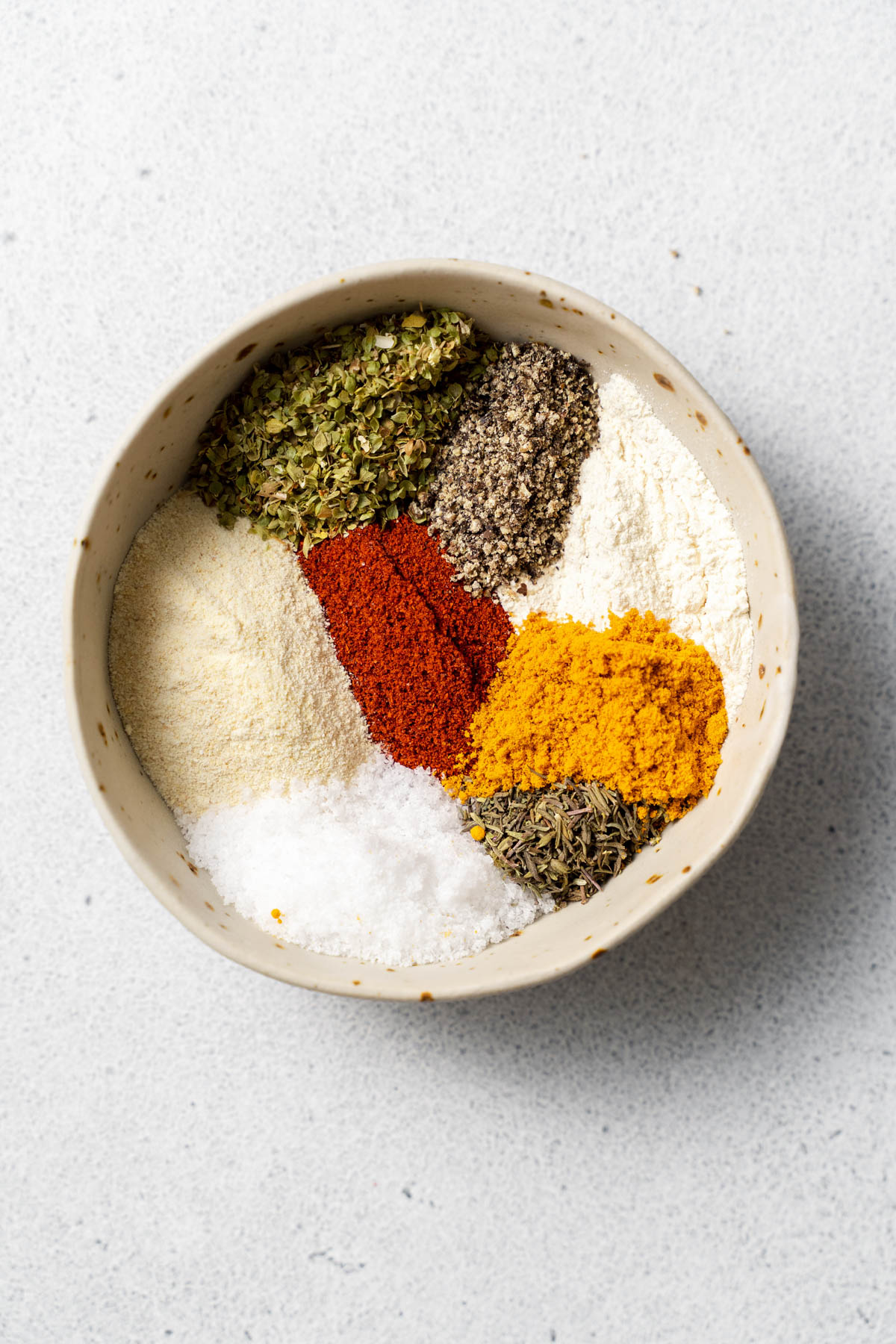 Overhead image of multiple spices in a bowl, separated into piles before mixing. 