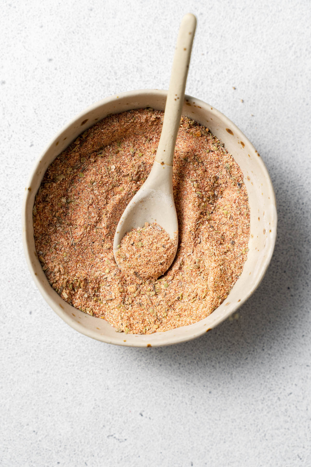 Overhead image of a bowl containing a spice blend. A spoon is inserted in the blend and is resting on the edge of the bowl. 