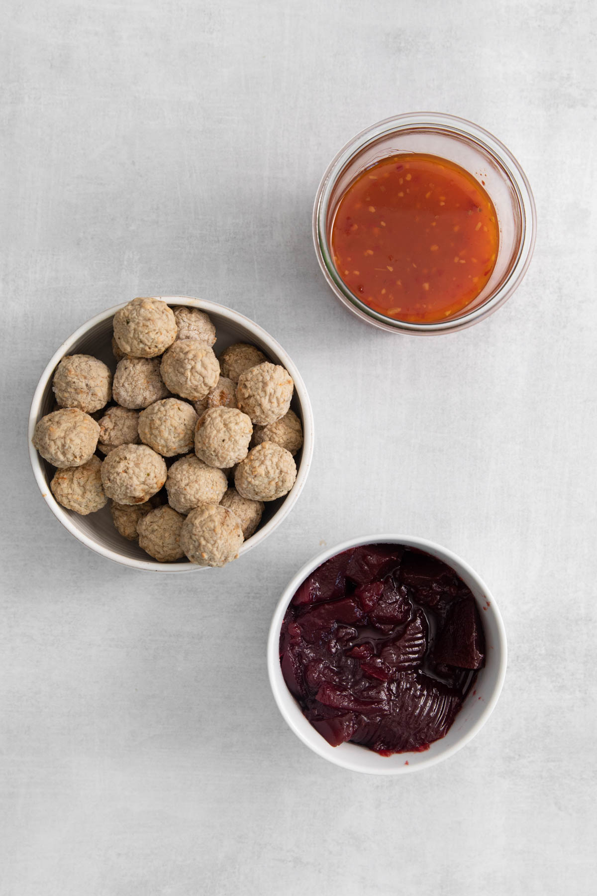 Overhead image of ingredients for cranberry crockpot meatballs, displayed in separate bowls. 