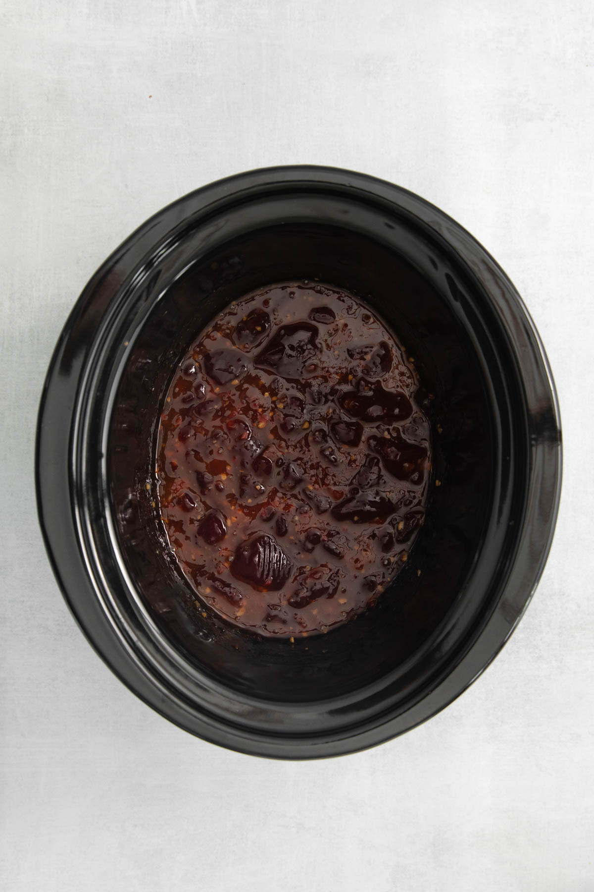 Overhead view of a crock pot filled with cranberry sauce and sweet chili sauce. 