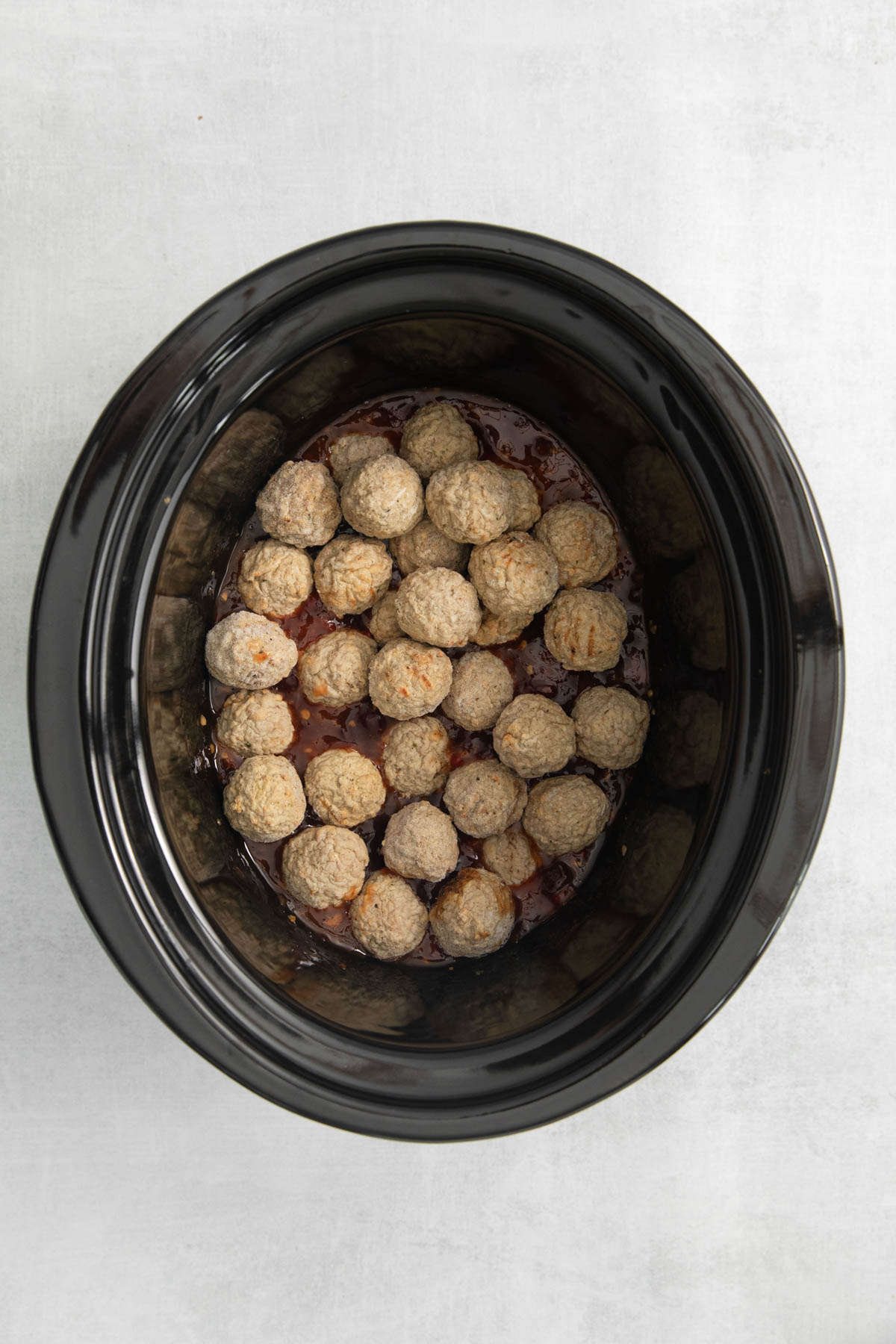 Overhead image of crock pot insert filled with frozen meatballs. 