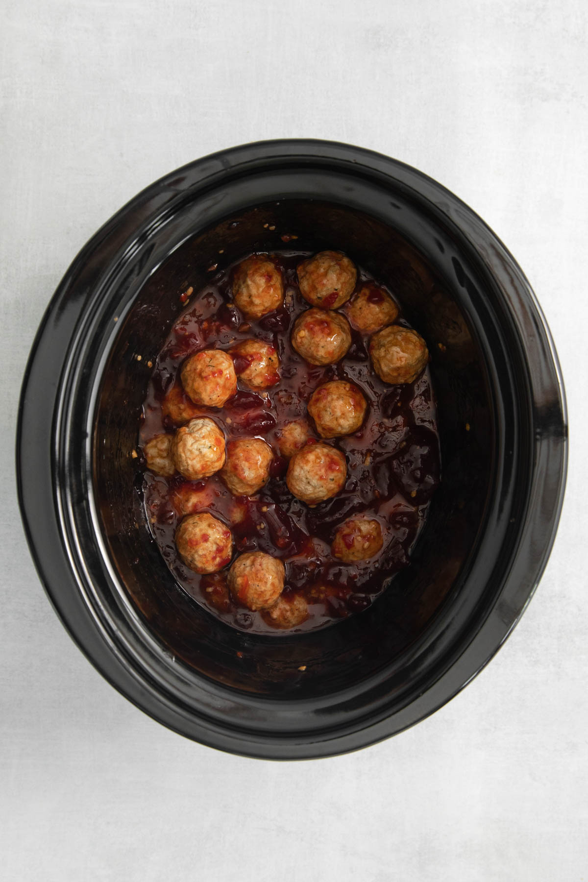 Cooked cranberry meatballs in a crock pot insert. 