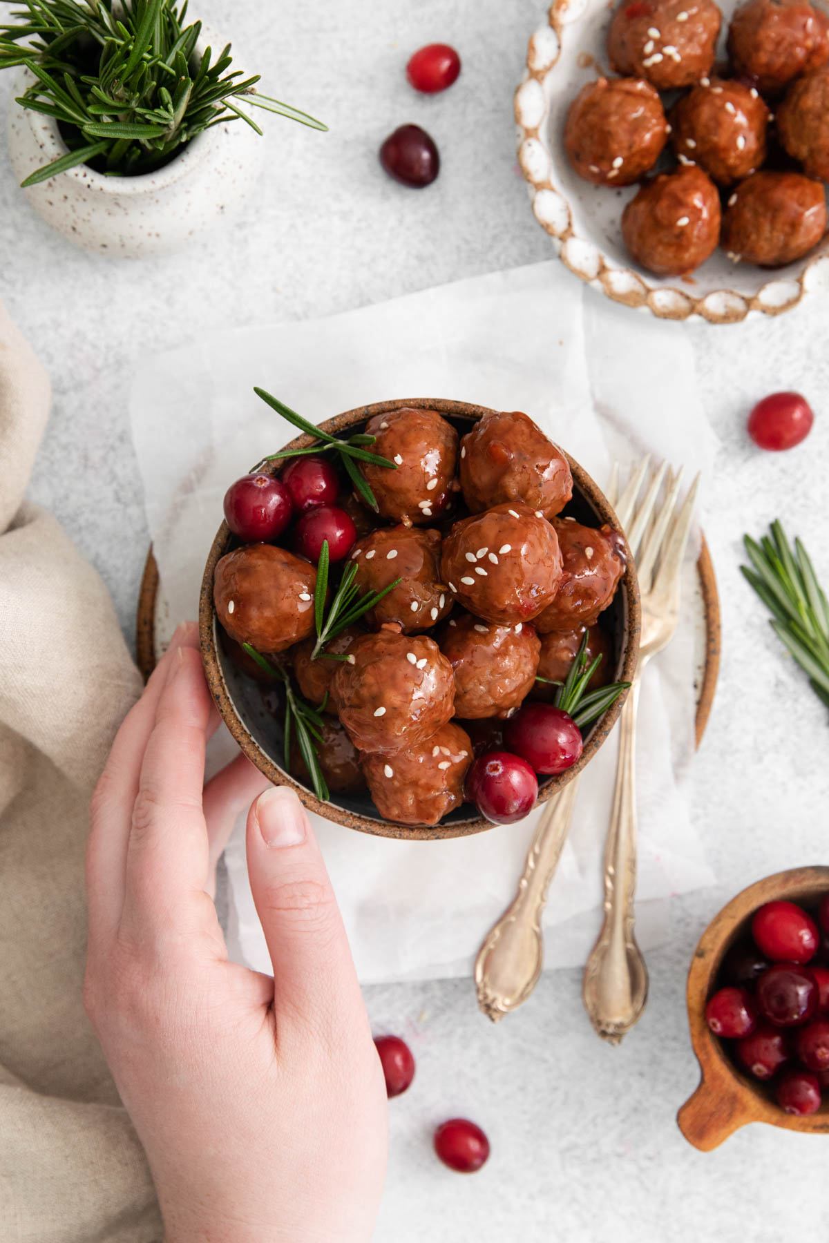 A hand is touching a bowl of cranberry meatballs. 