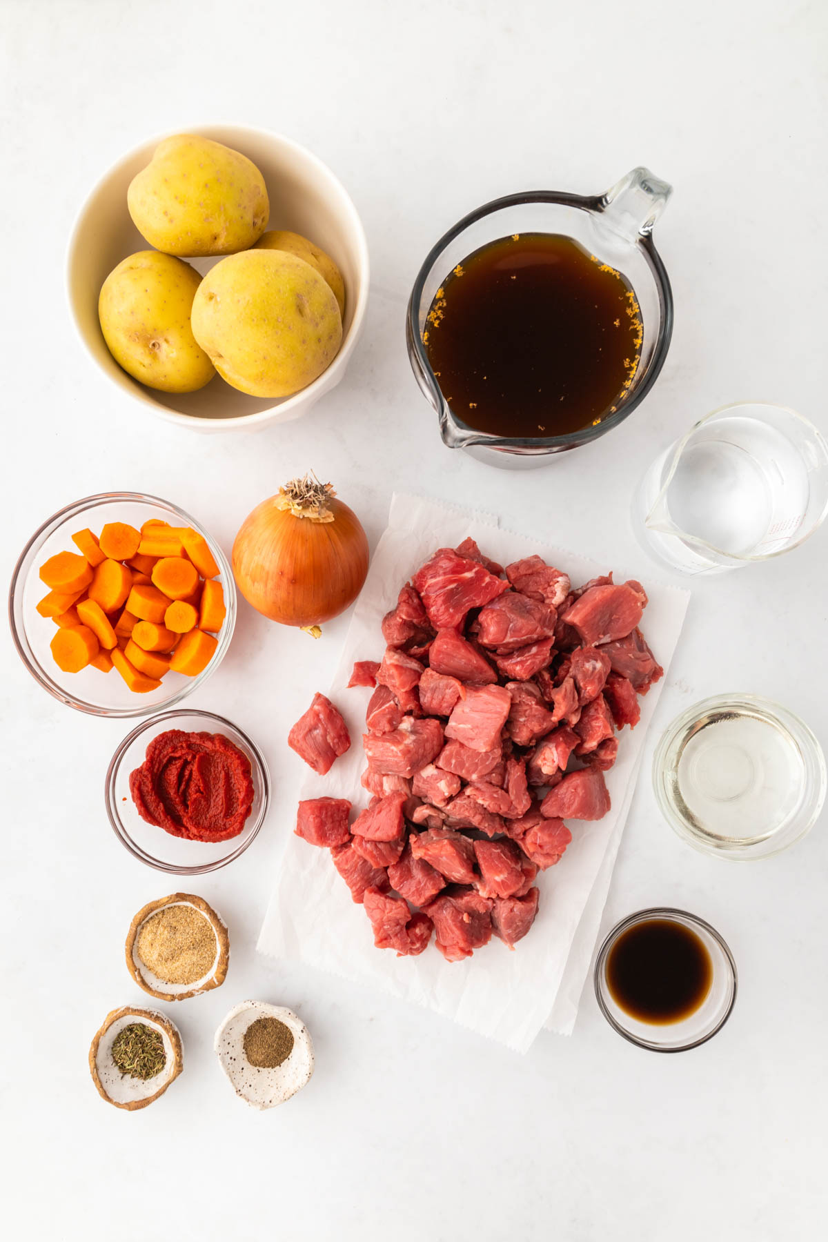 Overhead image of chopped beef on a cutting board, surrounded by chopped carrots, potatoes and spices in individual bowls. 