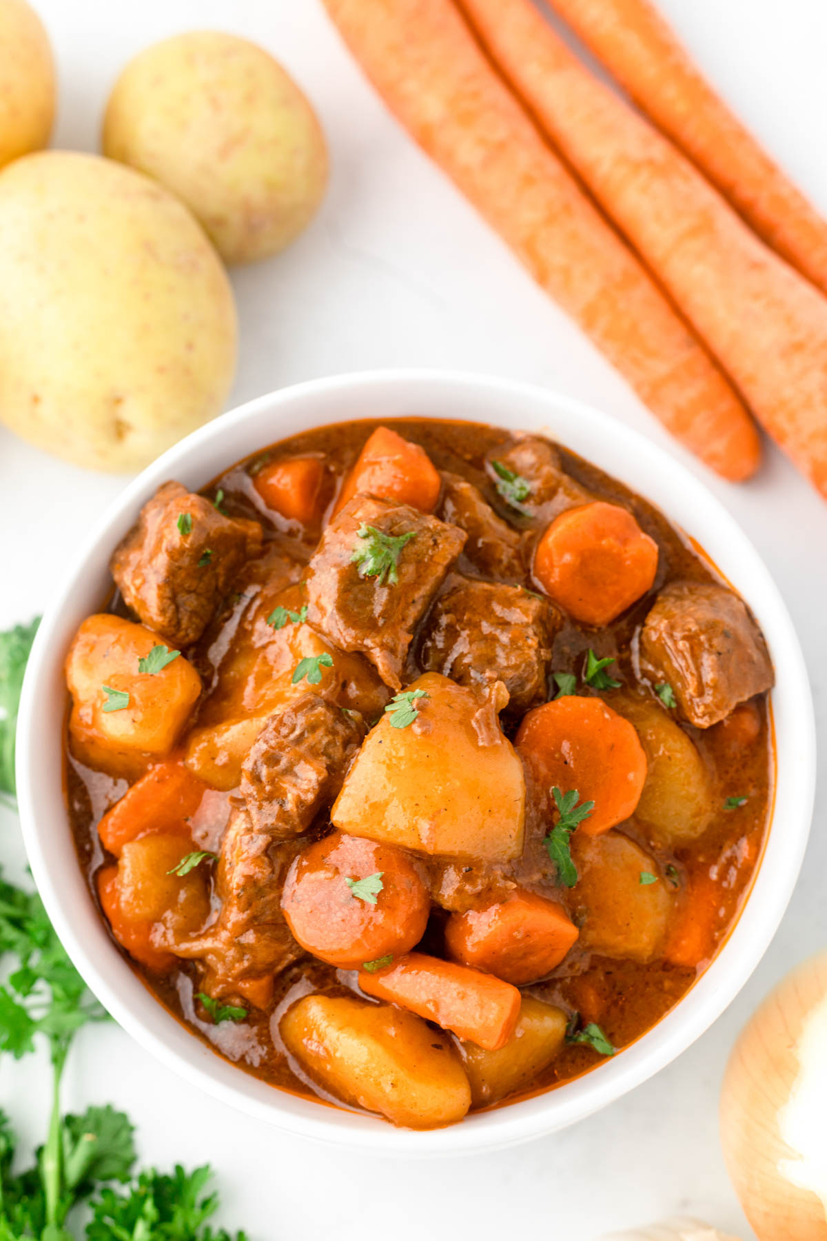 An overhead image of beef stew in a bowl with carrots, potatoes, onion and parsley visible. 