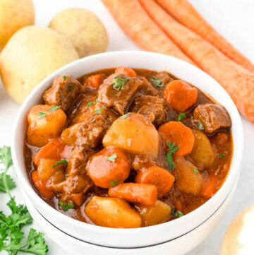 A bowl of beef stew next to vegetables.
