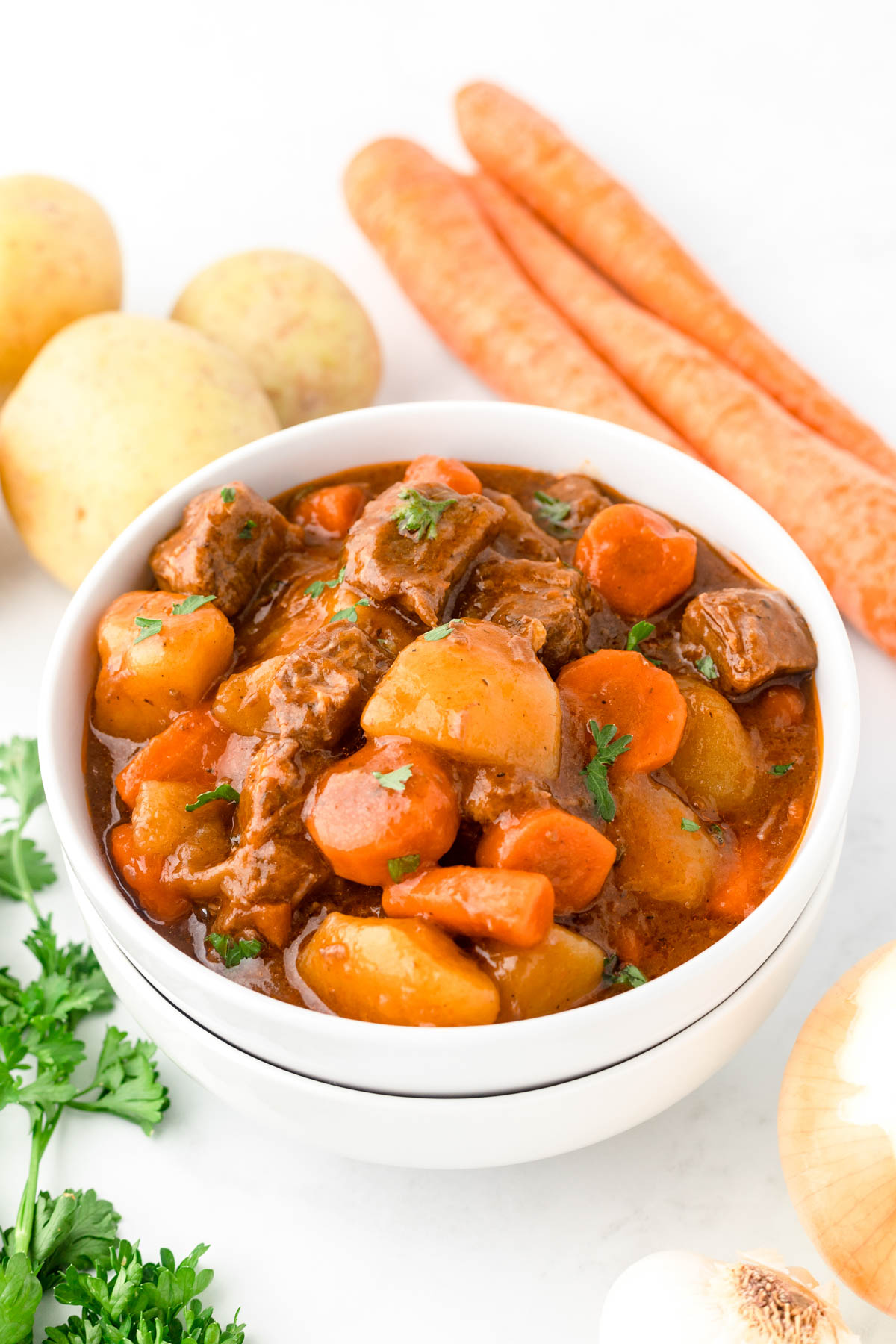 A bowl of beef stew next to vegetables.