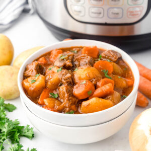 A bowl of beef stew in front of an instant pot.