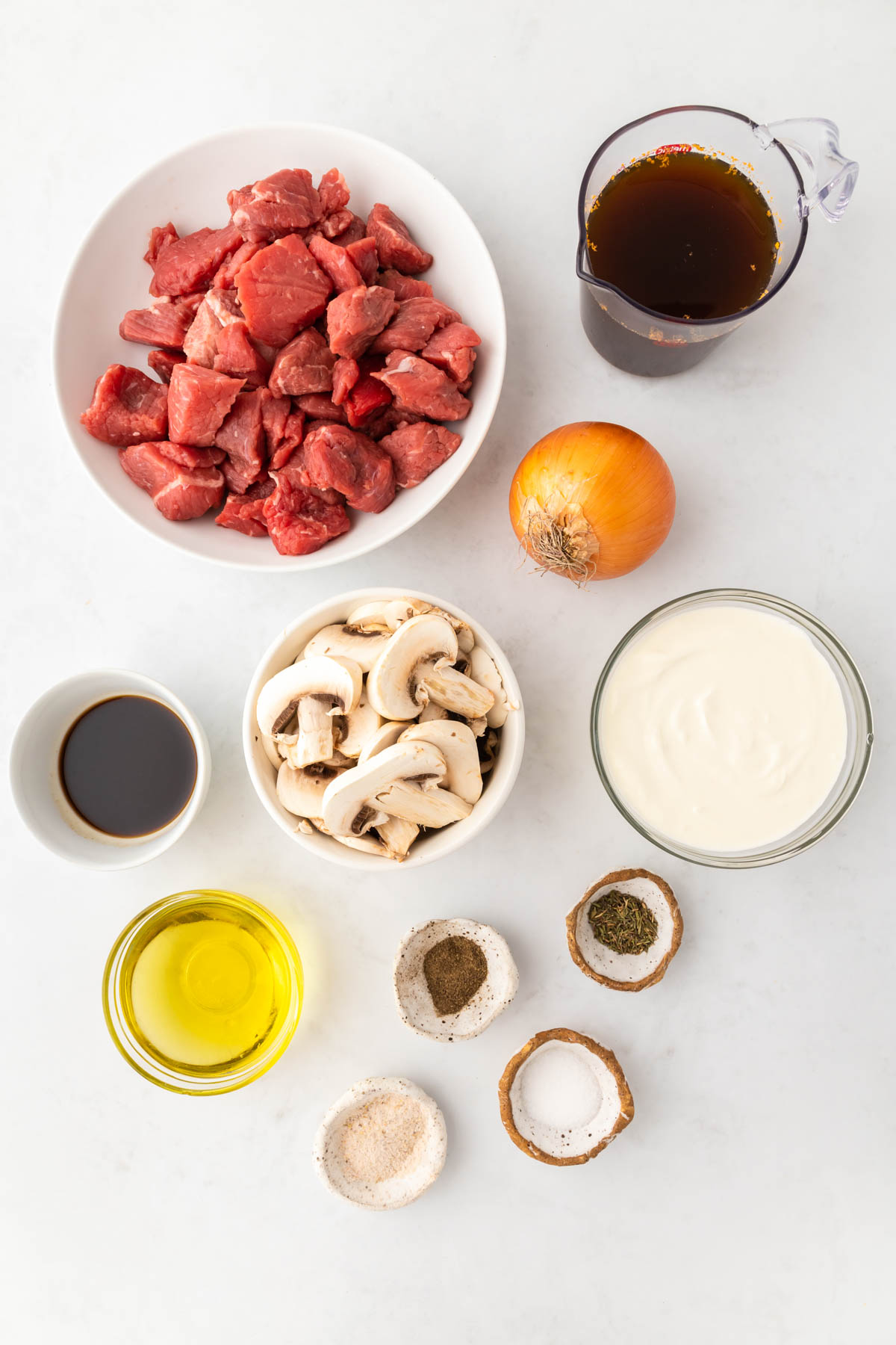 Beef cut into small chunks, mushrooms, spices and sauces are displayed in individual bowls. 