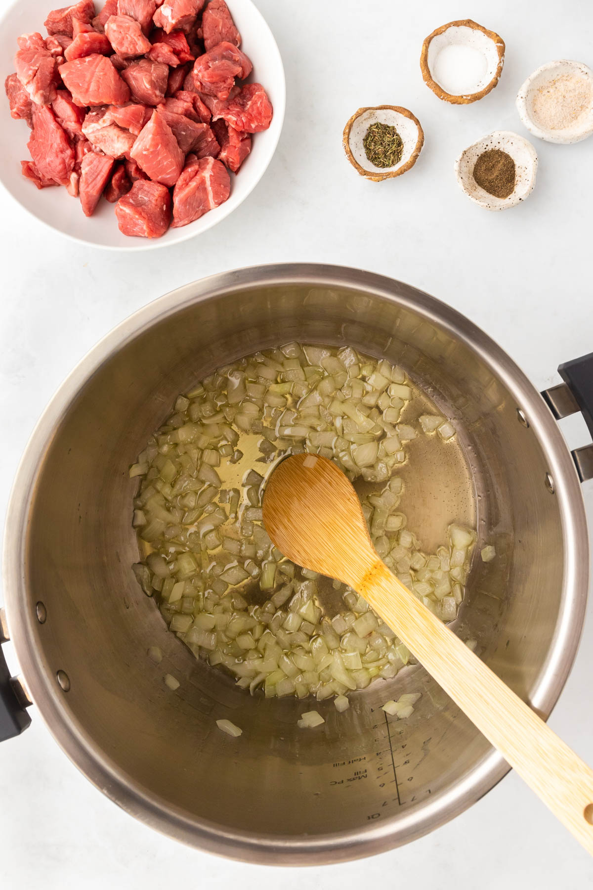 Minced onion and olive oil are combined in the insert of an instant pot, stirred with a wooden spoon.