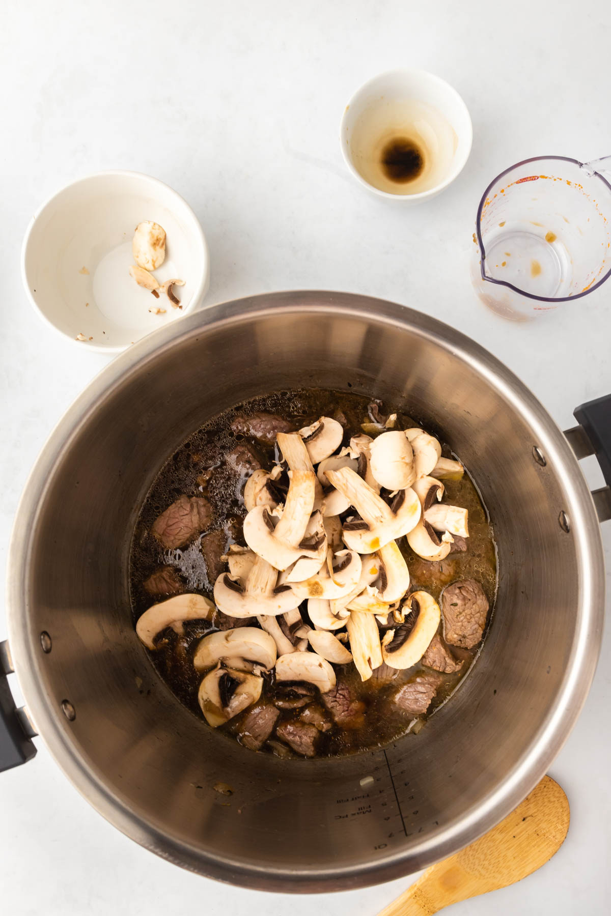 Mushrooms are added to cubed and browned beef in an Instant Pot insert.