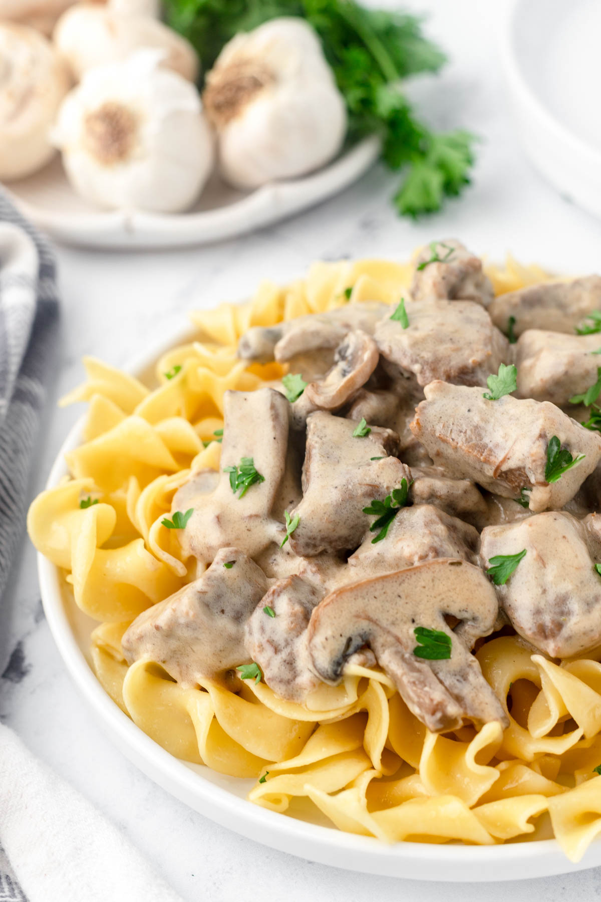 Beef stroganoff is sprinkled with chopped parsley and served on a bed of cooked egg noodles. 