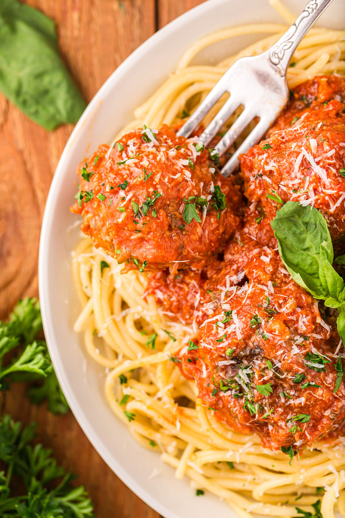 A fork piercing a meatballs on a plate of spaghetti.