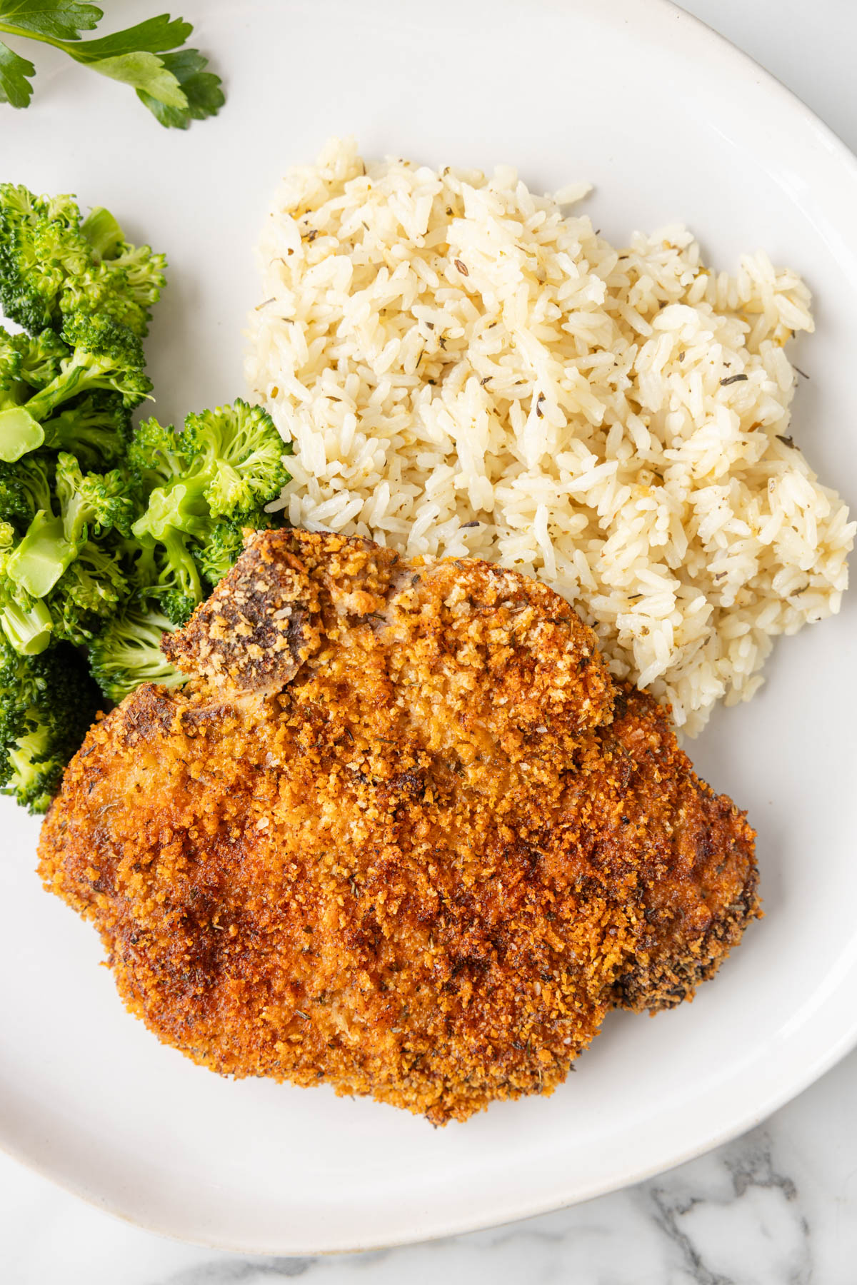Overhead view of baked pork chops, rice and broccoli served on a white plate. 