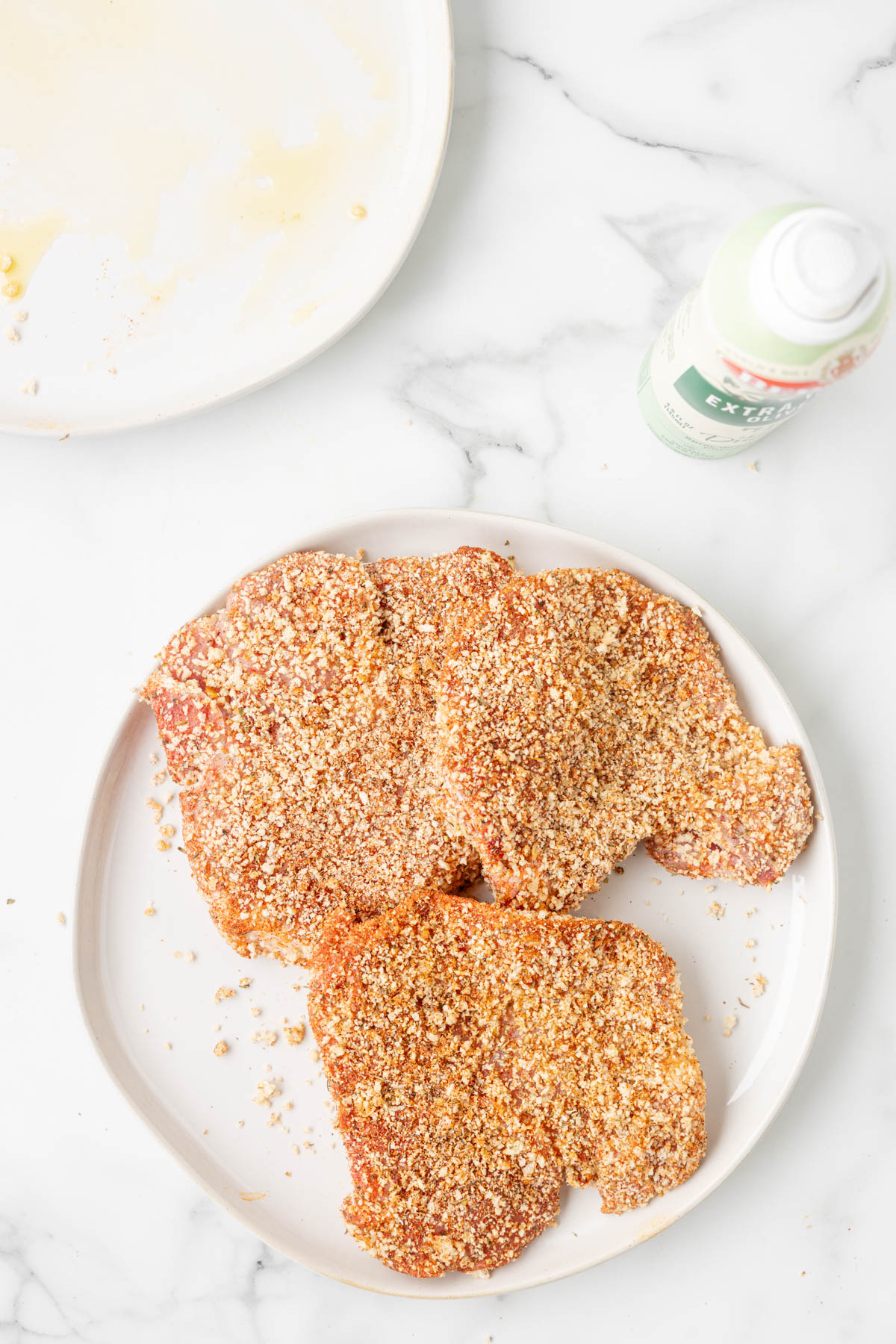 Uncooked pork chops are shown after being coated in a breadcrumb and spice mixture, ready for cooking. 