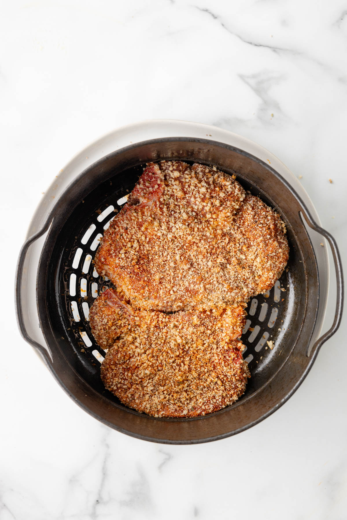 Pork chops are breaded and resting in an air fryer basket. 