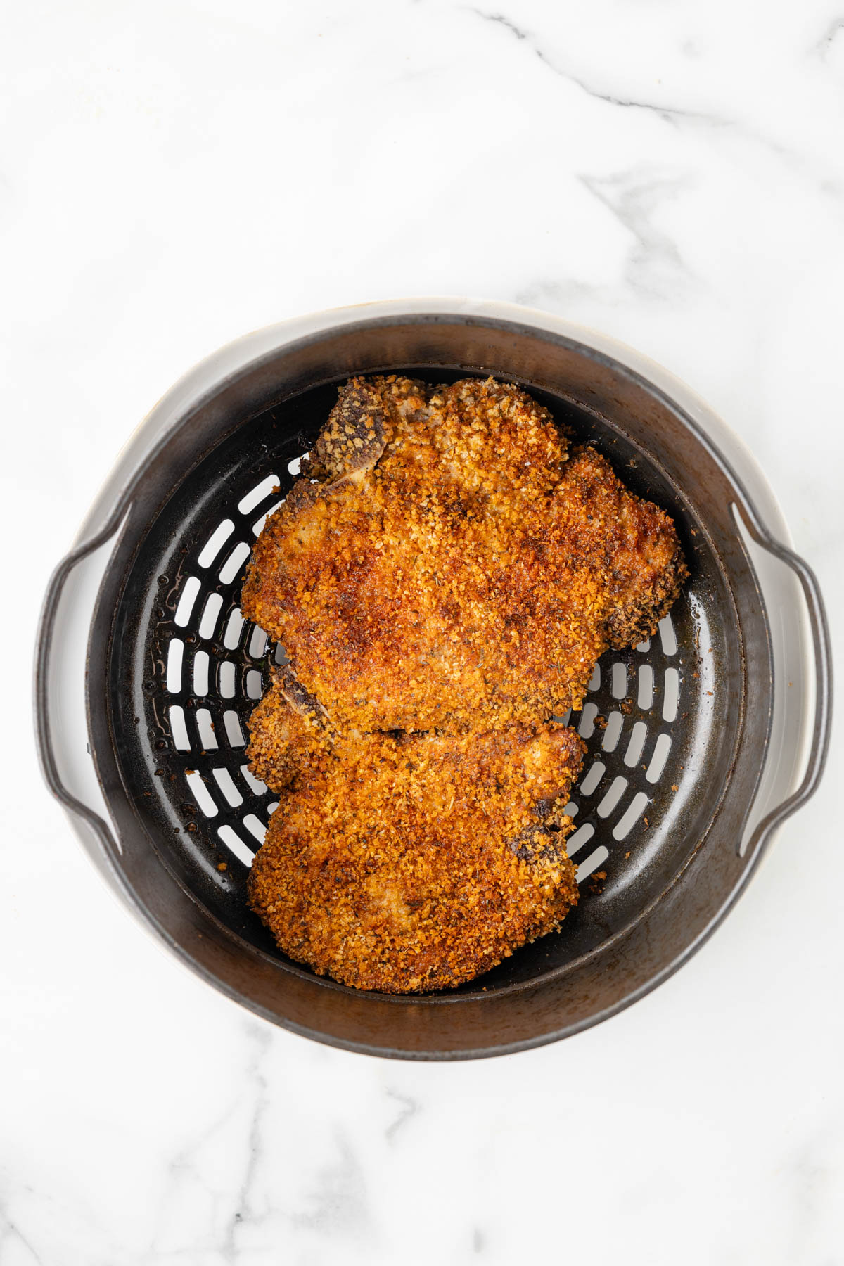 Air fryer fried pork chops are displayed in an air fryer basket. 