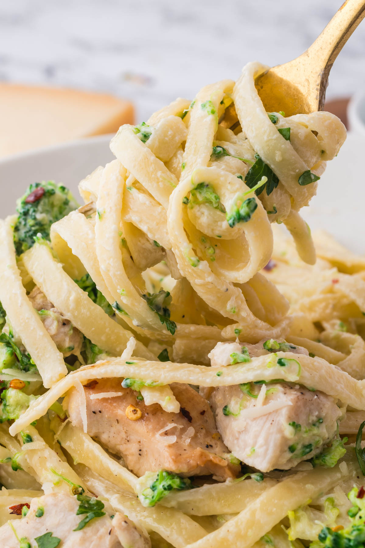 Closeup image of pasta noodles entwined on a gold fork, with broccoli bits and sauce visibly coating the noodles. 