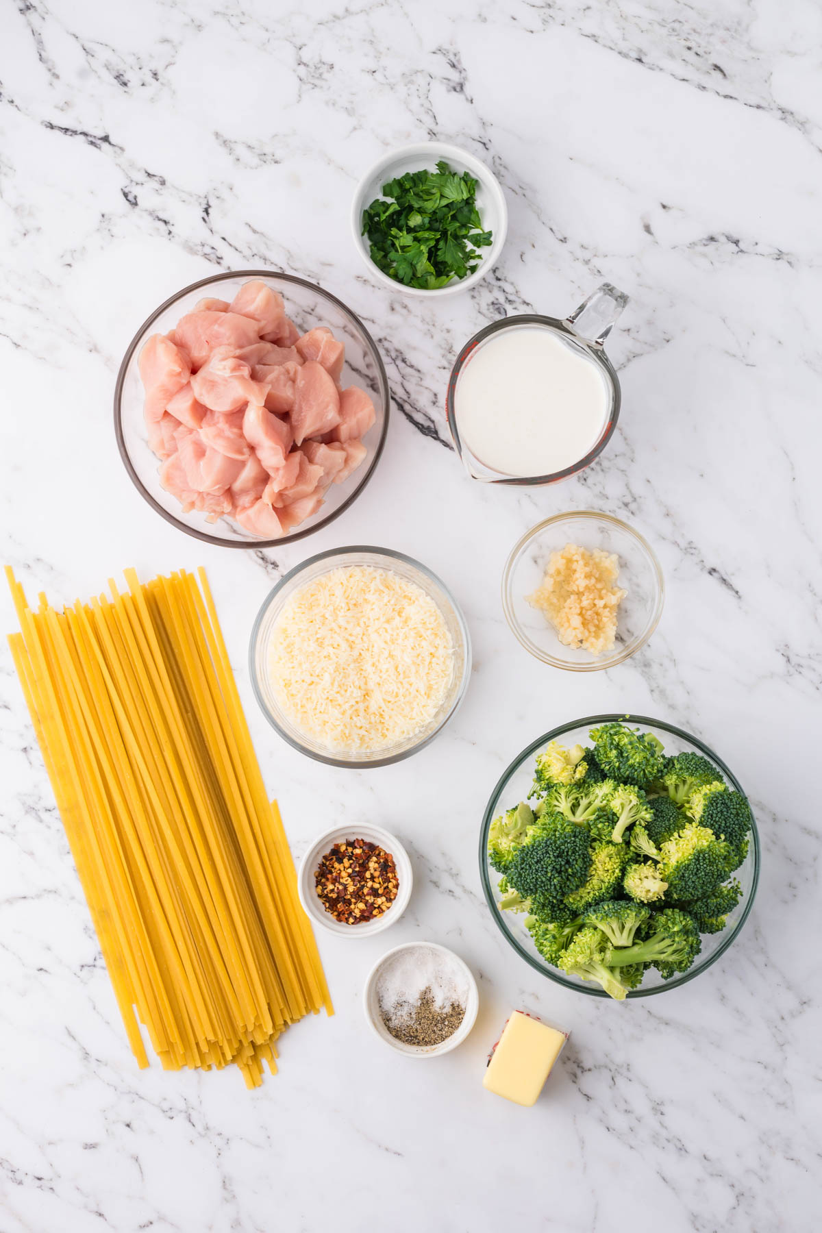 Overhead shot of ingredients in separate bowls displayed near uncooked fettuccini noodles. 