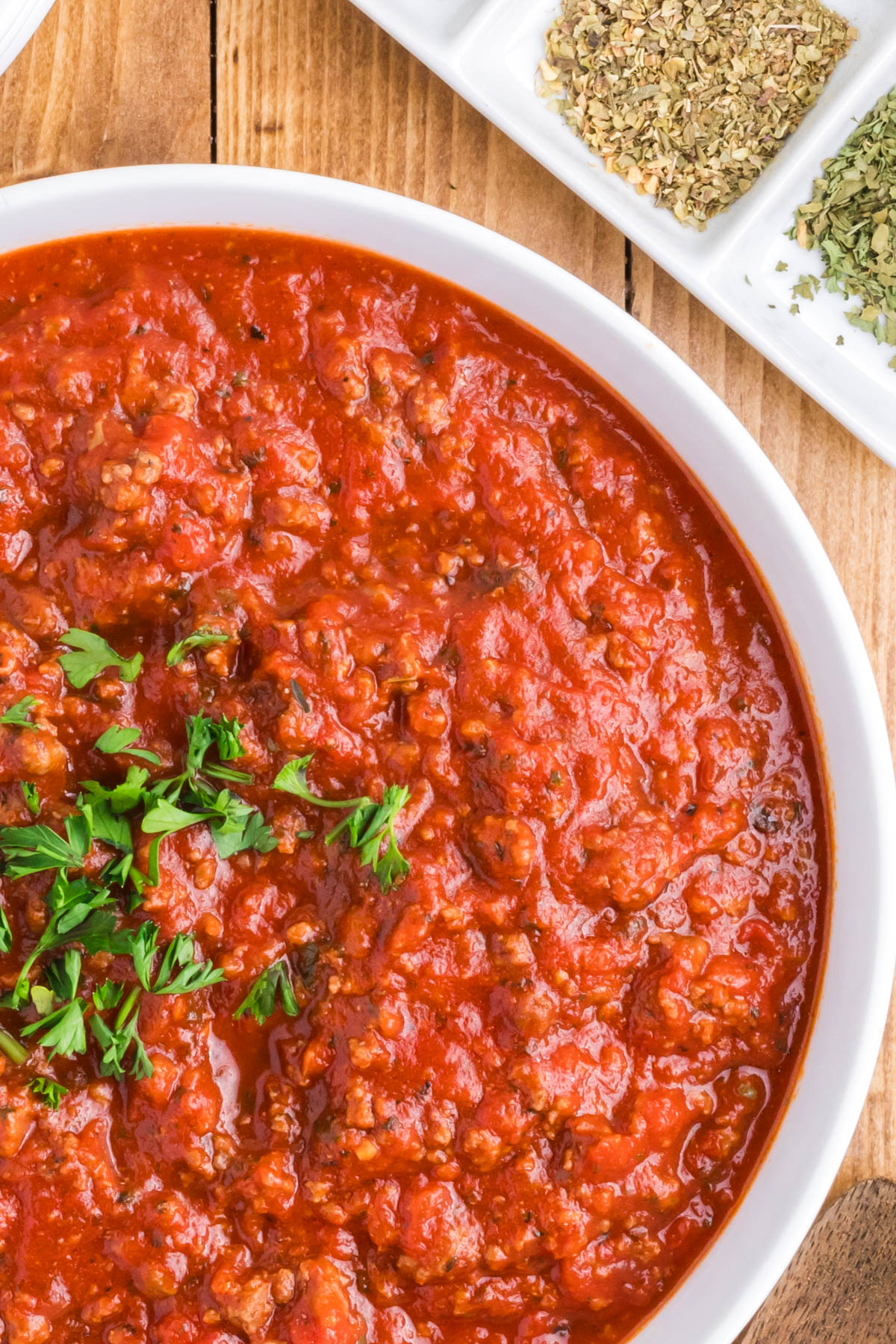 A close up image of meat sauce with chopped parsley sprinkled on top.