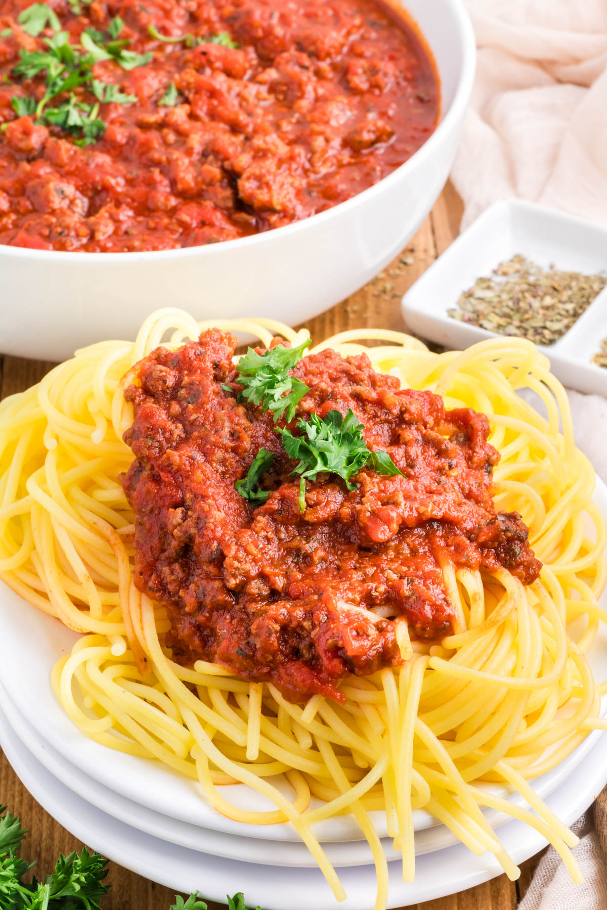 An image of a plate of spaghetti with meat sauce in front of a pan of meat sauce.