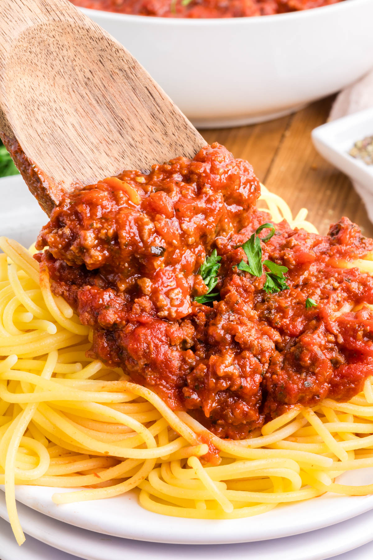 Spooning meat sauce onto cooked spaghetti.
