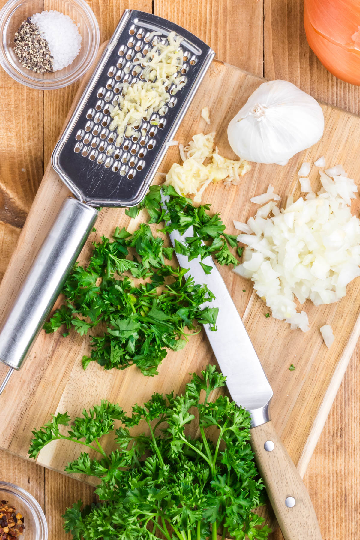 Chopped parsley, minced garlic, and onion on a cutting board.