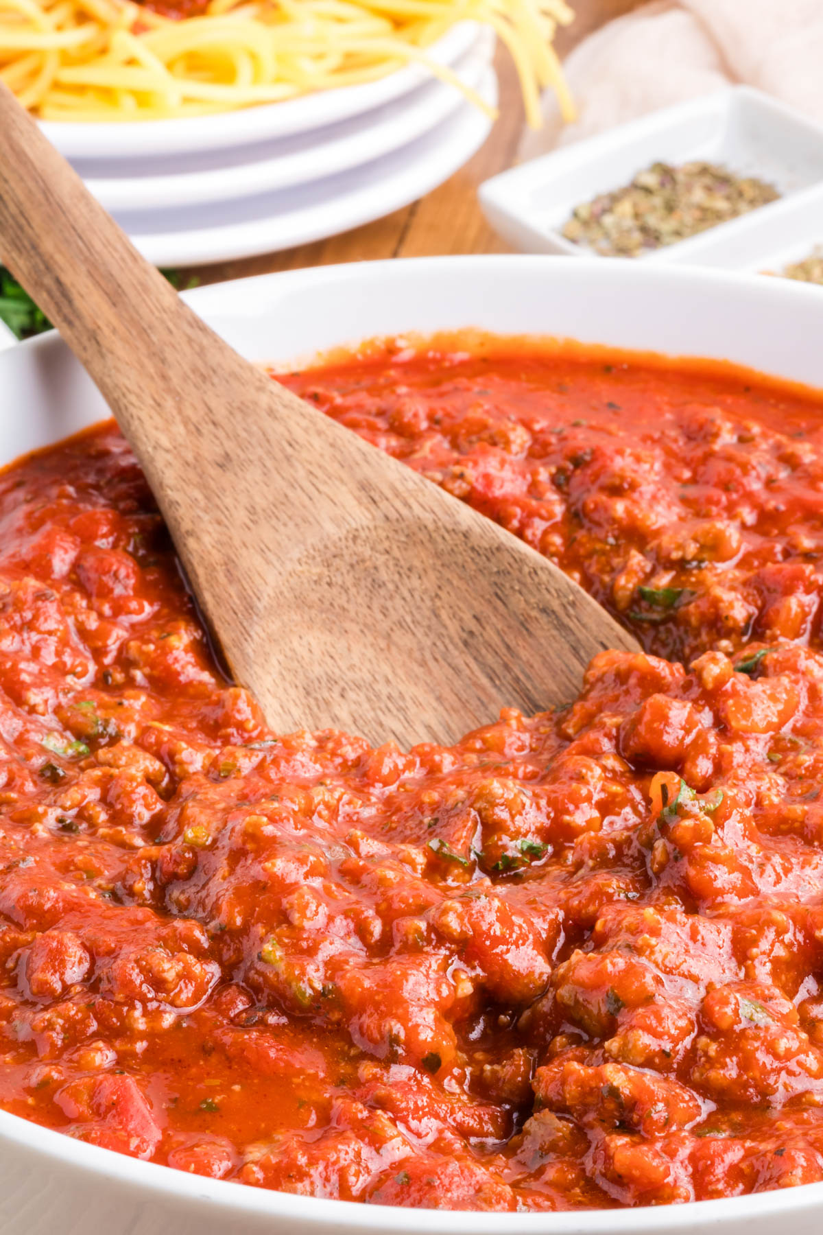 A wooden spoon in a pan of meat sauce.