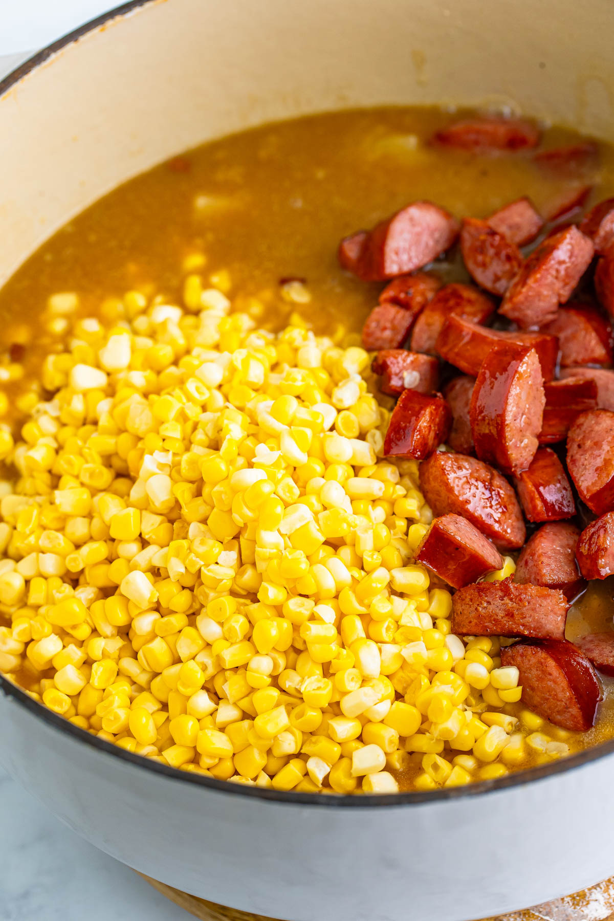 Fresh corn and browned kielbasa are added to chowder cooking in a large pot. 