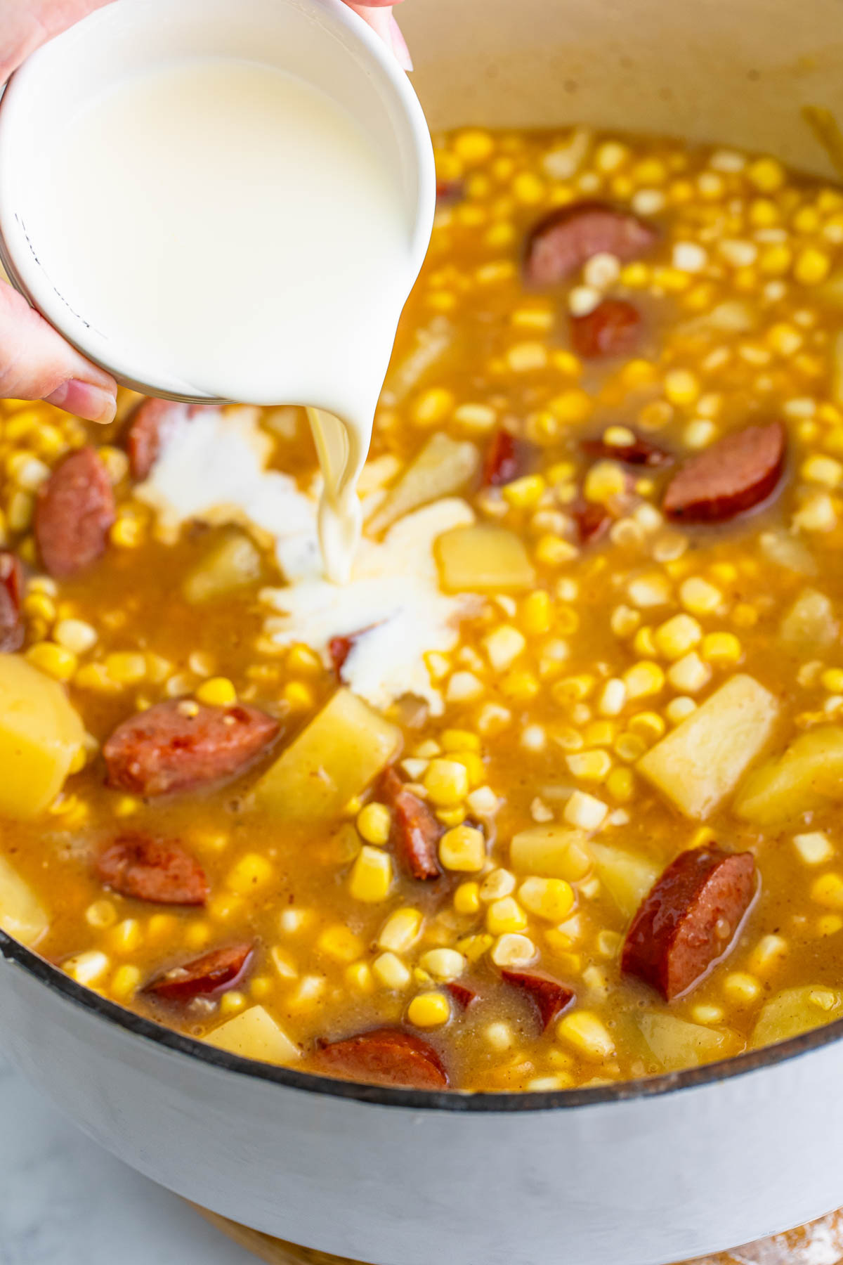 Heavy cream is poured in Kielbasa corn chowder. 