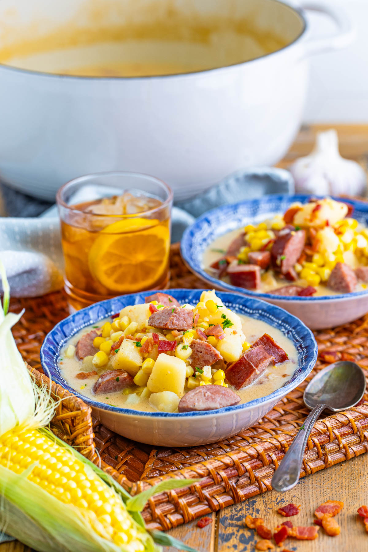 A table with soup bowls full of Kielbasa corn chowder, corn on the cob, and a large stock pot.