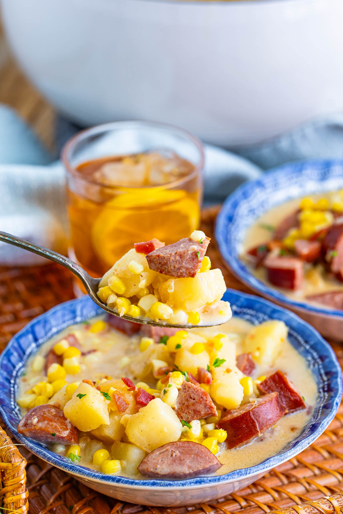 Close up of a spoonful of kielbasa corn chowder, with soup bowls visible in the background. 